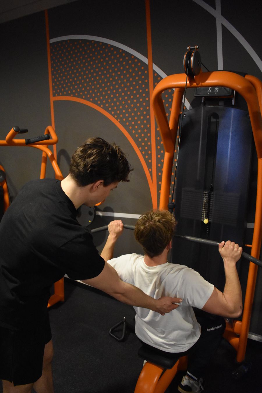 Jason corrigeert de houding van een klant tijdens de lat pulldown